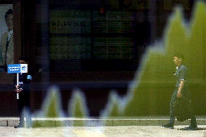 A man holding a signboard of a shareholders meeting and a pedestrian are reflected in an electronic board showing the graph of the recent fluctuations of the Japan's Nikkei average outside a brokerage in Tokyo
