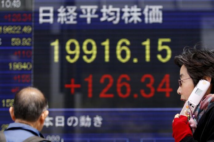 Pedestrians walk past an electronic board showing Japan's Nikkei average outside a brokerage in Tokyo