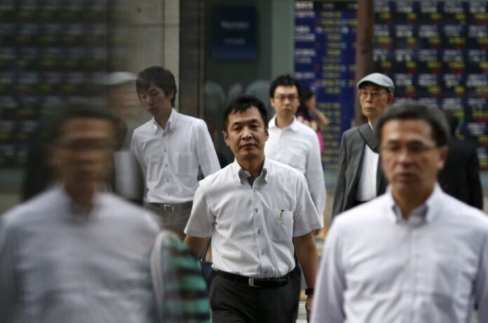 Pedestrians cross a road in front of an electronic board showing stock prices in Tokyo